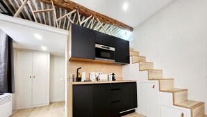 Une cuisine moderne avec des meubles noirs, un plan de travail en bois et un four à micro-ondes encastré. Un escalier en bois mène à l’étage supérieur.