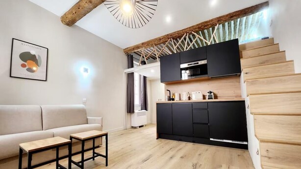 Un espace de vie moderne avec un escalier en bois, une cuisine dotée de meubles noirs, un canapé beige et une petite table en bois.