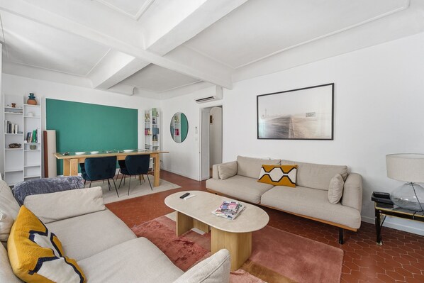 Un salon moderne comprenant un canapé, une table basse et un espace bureau avec des chaises.