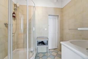 Une salle de bain avec une douche à parois de verre, une baignoire blanche et une petite étagère sur laquelle se trouve un objet noir.