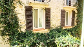 A stone building with two balconies, each with a metal railing and wooden shutters.
