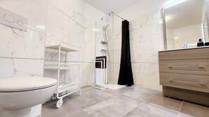 A modern bathroom with a toilet, a glass shower enclosure, a black shower curtain, and a wooden vanity with a mirror.