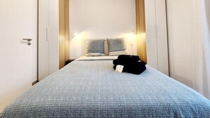 A narrow hotel room with a bed, two bedside tables, and a wardrobe.