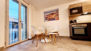 A modern kitchen with a built-in oven and microwave, a dining area with a table and chairs, and a large window with a view of the city.