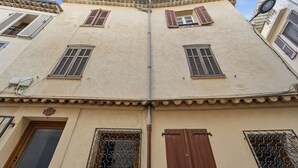 Ein Gebäude mit hellbeige Fassade, zahlreichen Fenstern mit Fensterläden und einem Ziegeldach.