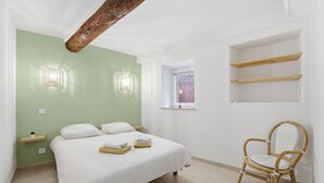 Ein Schlafzimmer mit Bett, Stuhl, Fenster und integrierten Regalen.
