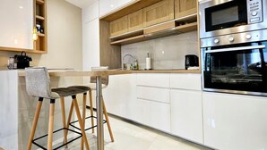 A modern kitchen with white cabinets, wooden accents, a built-in oven, and a bar area with stools. - Le Championnet - Proche du Port (Antibes)