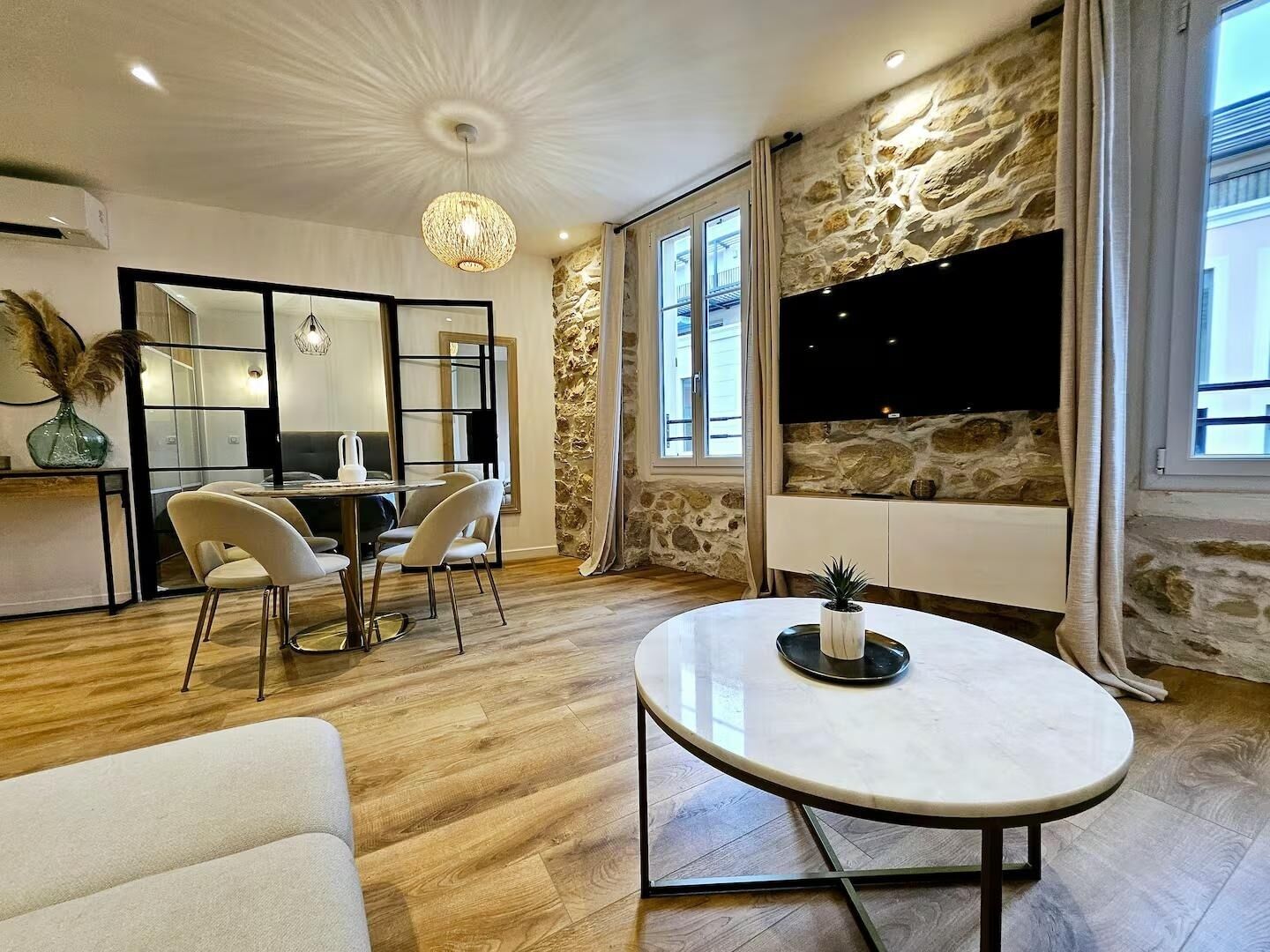 A modern living room with a stone accent wall, a dining area with a round table, and a large TV mounted on the wall.