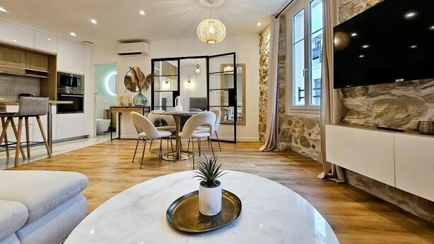 A modern living room with a marble coffee table, a stone accent wall, and a large TV. - Le Championnet - Proche du Port (Antibes)