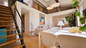 A modern living room with a staircase, a dining area, and a large plant. - Le Delmas Riviera - Duplex dans Vieil Antibes (Antibes)