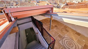 A rooftop terrace with a view of a cityscape, including terracotta-tiled buildings and a distant mountain range.