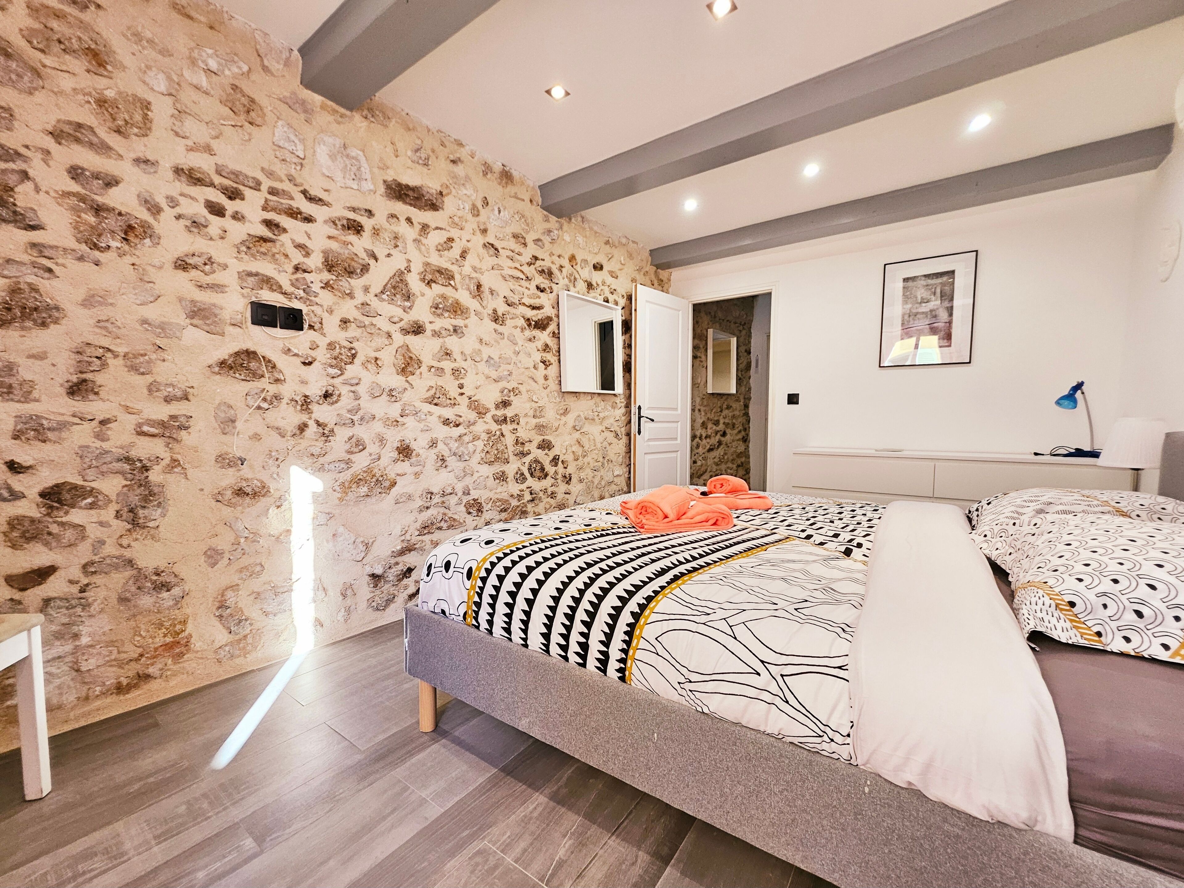 Una camera da letto con parete in pietra, un letto con copriletto decorato, un comodino con lampada e un quadro incorniciato appeso al muro.