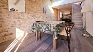 A dining area with a stone wall, wooden table, and chairs. There is a staircase and a lamp in the room.