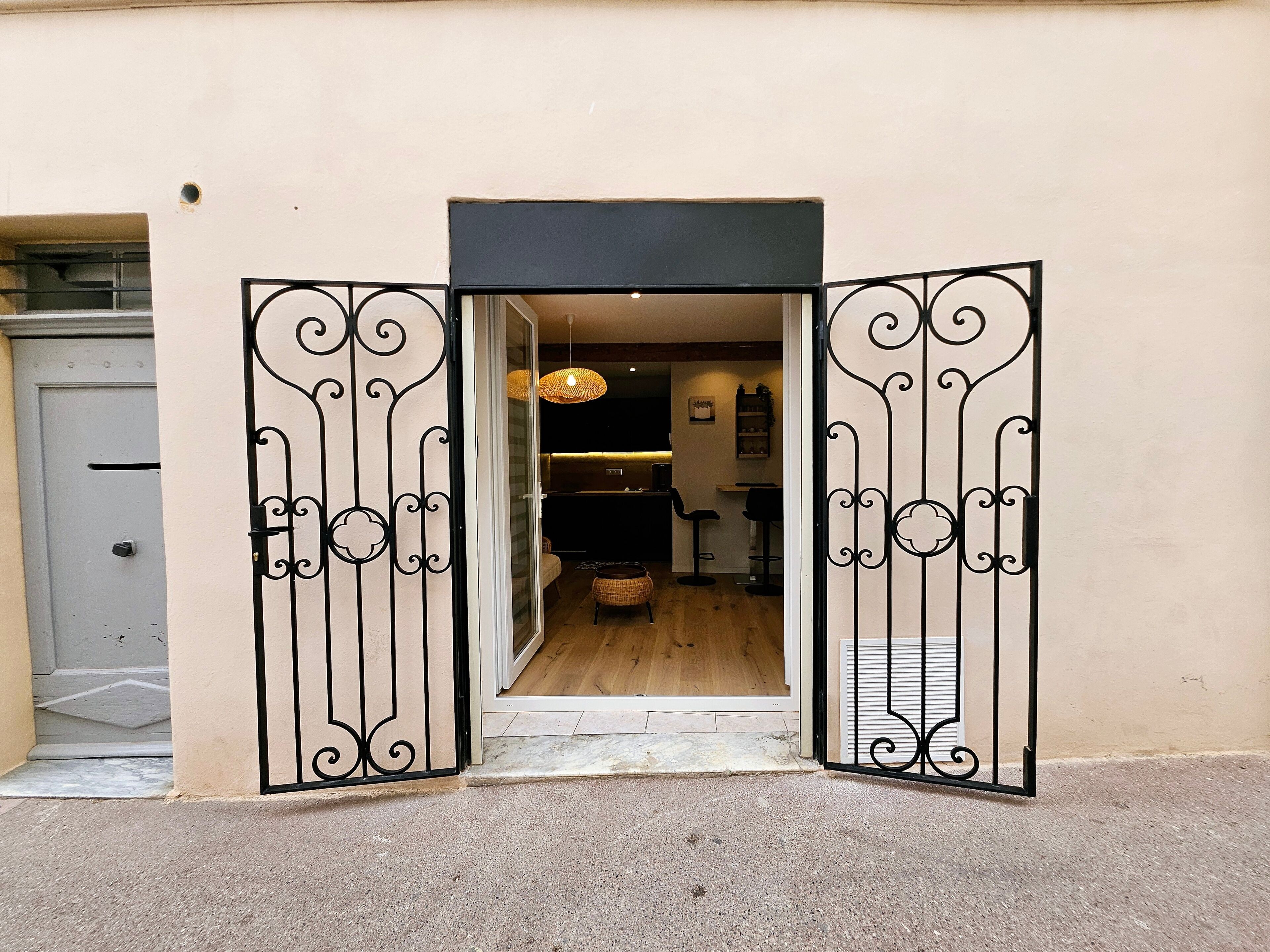 A doorway with ornate black metal gates leading to a room with a wooden floor and a hanging light fixture.