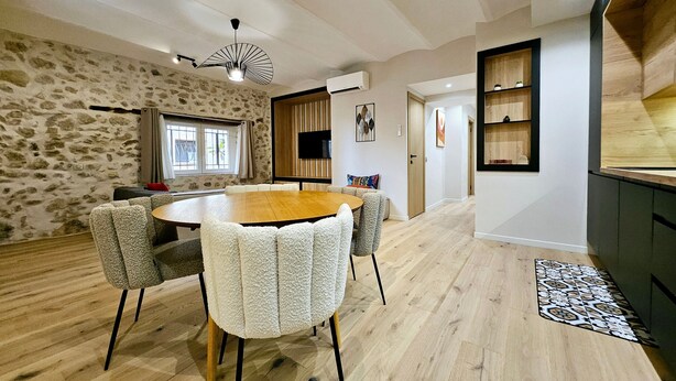 A modern dining area with a round wooden table, cushioned chairs, and a stone wall.