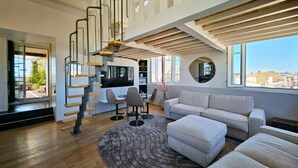 A modern living room with a staircase, a sofa, a coffee table, and a TV. - Le Phare Azur - T3 avec Vue Mer (Antibes)