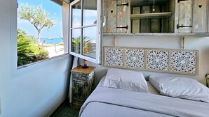 A bedroom with a large window, a bed, a decorative headboard, and a small wooden nightstand. - Le Phare Azur - T3 avec Vue Mer (Antibes)