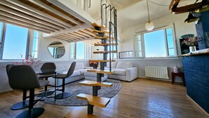 A spacious living area with a modern staircase, a dining table with chairs, and a sofa. - Le Phare Azur - T3 avec Vue Mer (Antibes)
