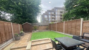 A backyard with a lawn, patio furniture, a wooden shed, and a brick wall.