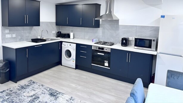 Une cuisine moderne avec des meubles de couleur sombre, un lave-linge, un four à micro-ondes et une cuisinière.