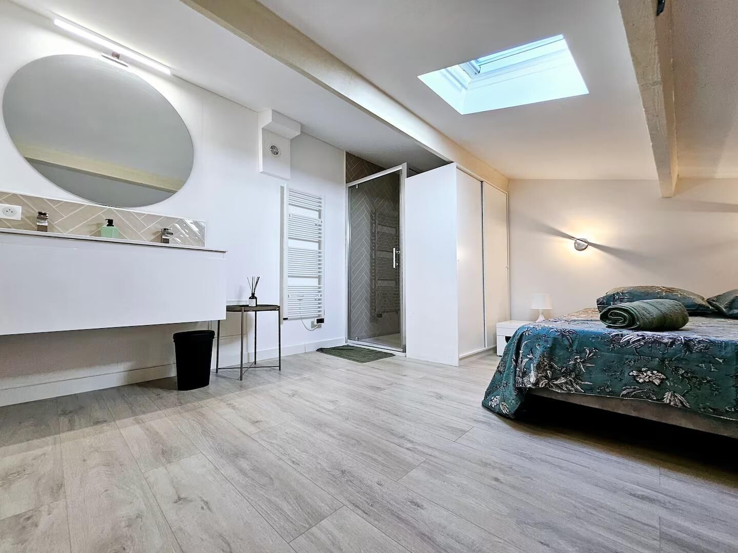 A modern bedroom with a skylight, a large mirror, a bedside table, and a bed with a floral bedspread.