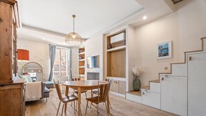 A modern kitchen with wooden cabinets, a dining table, and chairs. There is a staircase with a wooden railing leading to an upper floor.