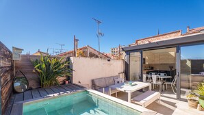 A rooftop pool area with a glass-enclosed kitchen, outdoor seating, and a wooden deck.