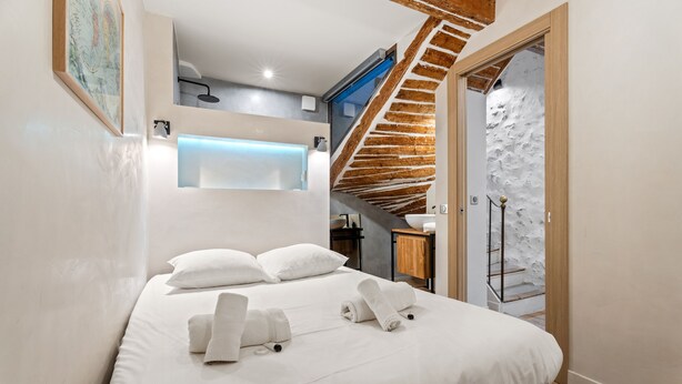 A modern bedroom with a large bed, a wooden staircase, and a bathroom with a modern sink.