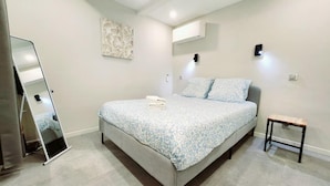 Une chambre à coucher comprenant un lit, une table de chevet, un miroir et un climatiseur fixé au mur.