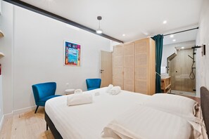 Habitación de hotel con una cama, dos sillas azules, un panel de madera, un baño con un espejo y un cartel en la pared.