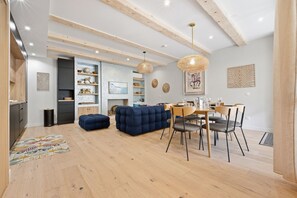 Un interior moderno con zona de comedor, asientos tapizados en azul, pisos de madera y una cocina con muebles oscuros.