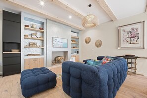 Una sala de estar moderna con chimenea, asientos tapizados en azul, estanterías de madera y objetos decorativos.