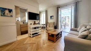 A modern living room with a wooden herringbone floor, a flat-screen TV, a sofa, a coffee table, and a chair.