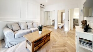 A modern living room with a light-colored sofa, a wooden coffee table, and a white cabinet with a flat-screen TV.