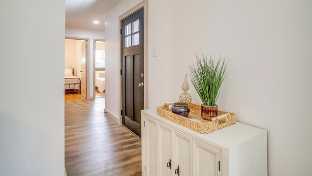A hallway with a wooden floor, a white cabinet with decorative items, and a door leading to another room. - Robin House with two master suites! (Burleson)