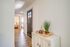 A hallway with a wooden floor, a white cabinet with decorative items, and a door leading to another room. - Robin House with two master suites! (Burleson)