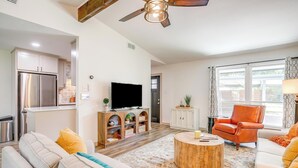 A modern living room with a sofa, coffee table, and orange chair. There is a TV, wooden cabinet, and a window with curtains. - Robin House with two master suites! (Burleson)