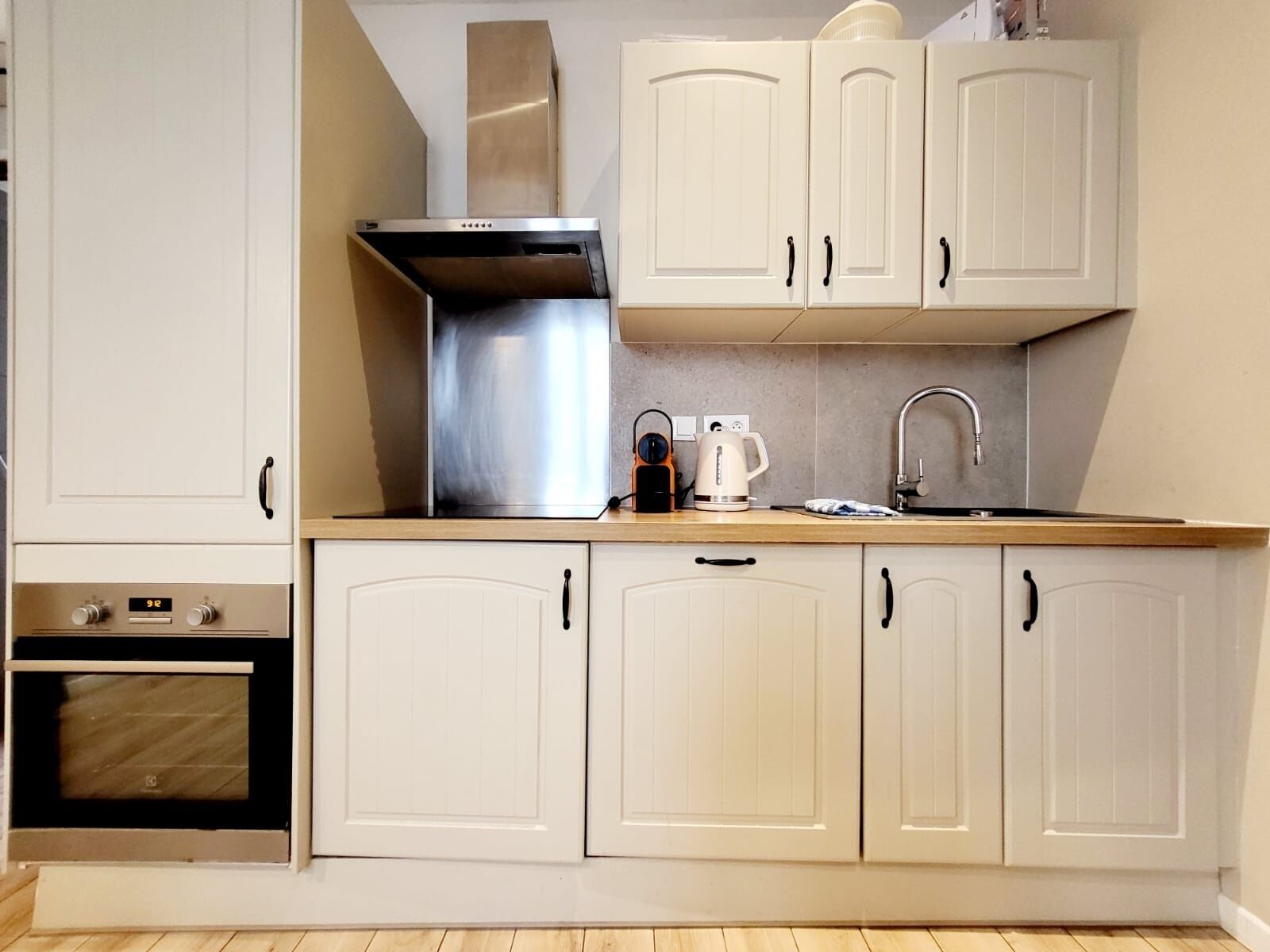 A kitchen with white cabinets, a stainless steel range hood, a coffee maker, and a built-in oven.
