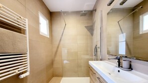 Ein modernes Badezimmer mit begehbarer Dusche, einem großen Spiegel und einem weißen Waschbecken.