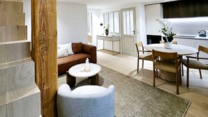 A spacious living area with a high ceiling, a staircase with wooden accents, a cozy seating area with a sofa and armchairs, a dining table with chairs, and a kitchen area with a sink and countertop. - Le Lacan - Proche du Port (Antibes)