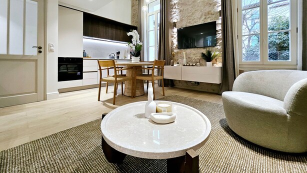 A modern living room with a round marble coffee table, a sofa, and a dining area with a wooden table and chairs. - Le Lacan - Proche du Port (Antibes)