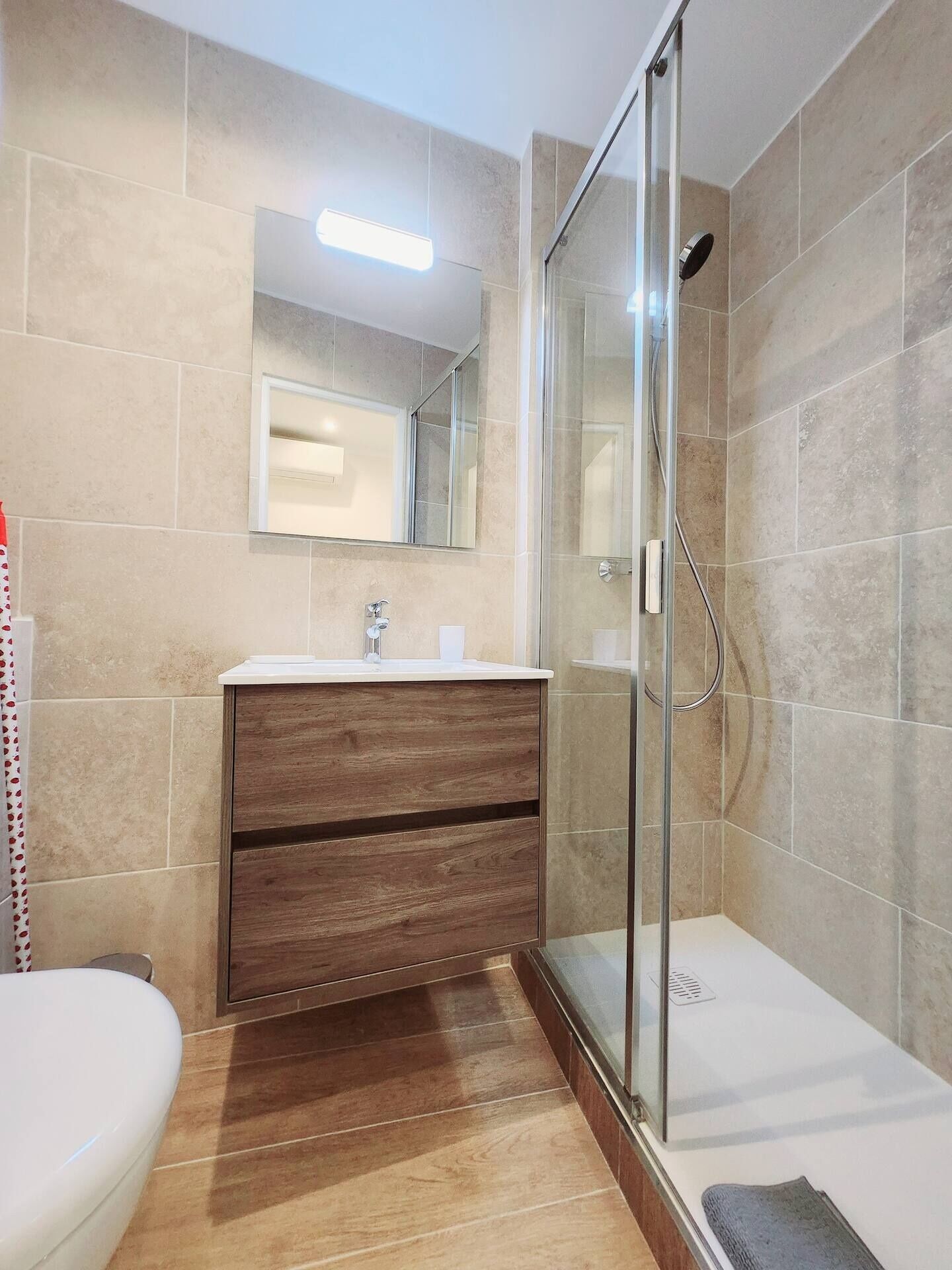 Un baño con cabina de ducha de vidrio, tocador de madera y lavabo blanco.
