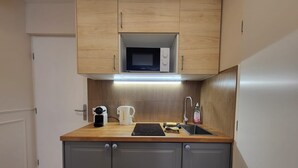 Una cocina compacta con armarios de madera, microondas, cafetera, lavamanos y una pequeña encimera.