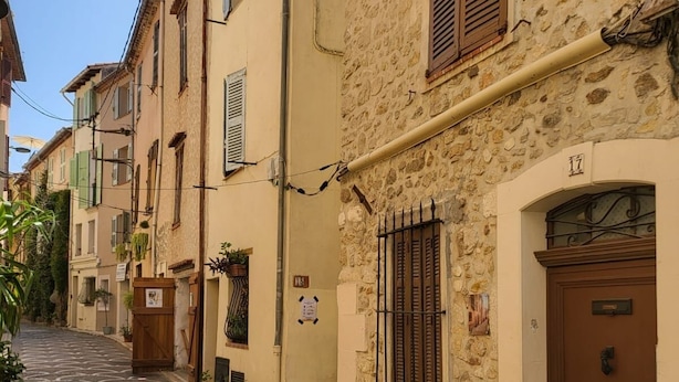 Una estrecha calle adoquinada flanqueada por edificios tradicionales, con una puerta que tiene una reja metálica y una placa con un número.