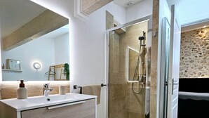 A modern bathroom with a wooden vanity, a glass shower enclosure, and a stone accent wall.