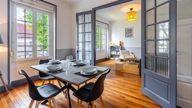 A dining area with a wooden table set for four, surrounded by black chairs.