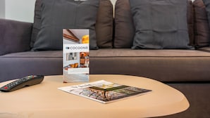 A remote control and a magazine on a round table in front of a sofa with multiple cushions.