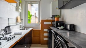 A compact kitchen with a gas stove, sink, and modern appliances. A window provides natural light, and a potted plant adds greenery.