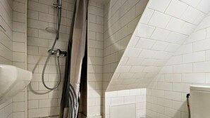 A bathroom with white tiled walls, a wooden floor, a shower with a curtain, a sink, and a toilet. - L'Hacienda RDC - climatisé proche de la plage (Antibes)