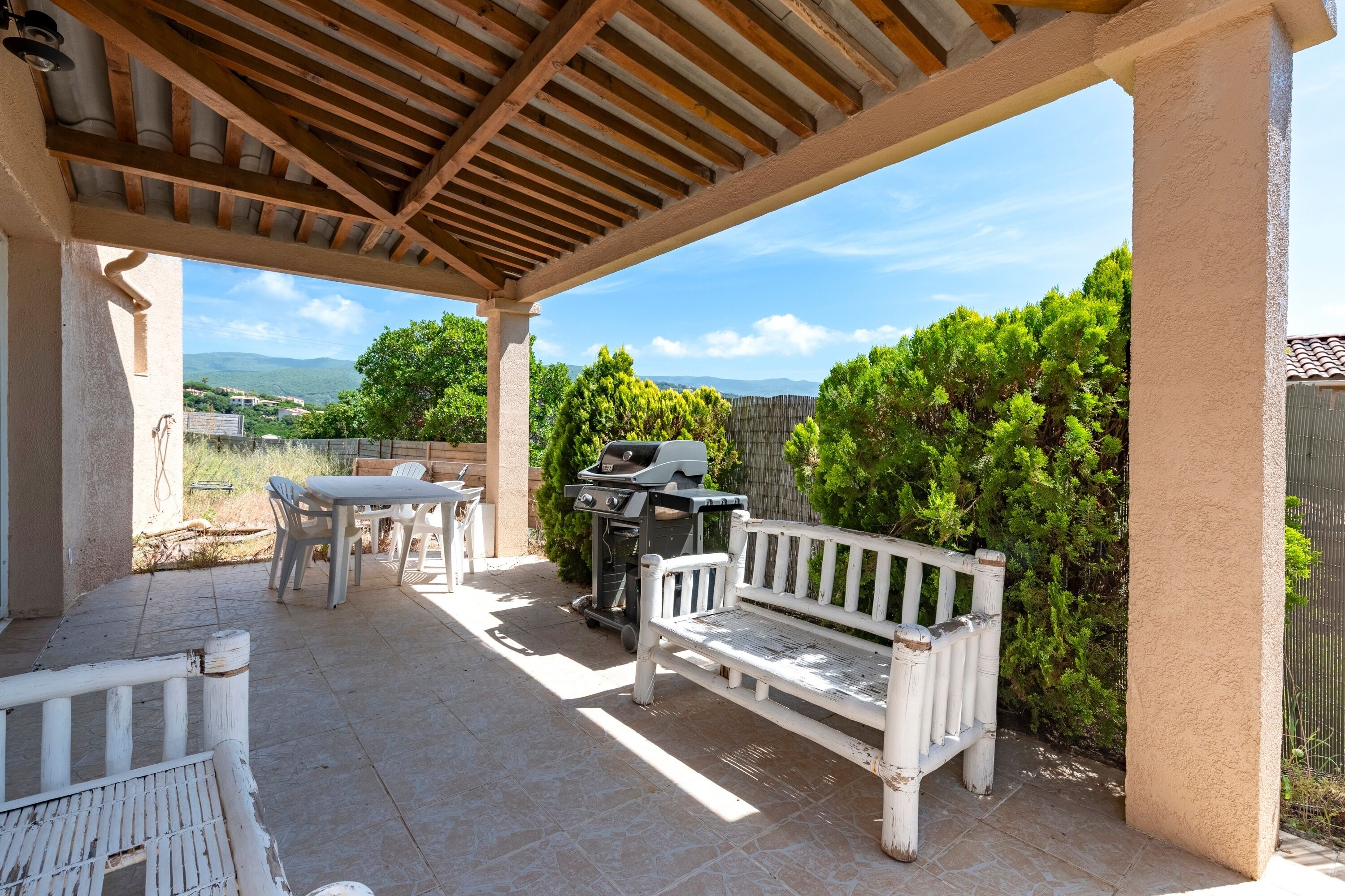 An outdoor patio with a wooden pergola, a grill, a white bench, and a table.